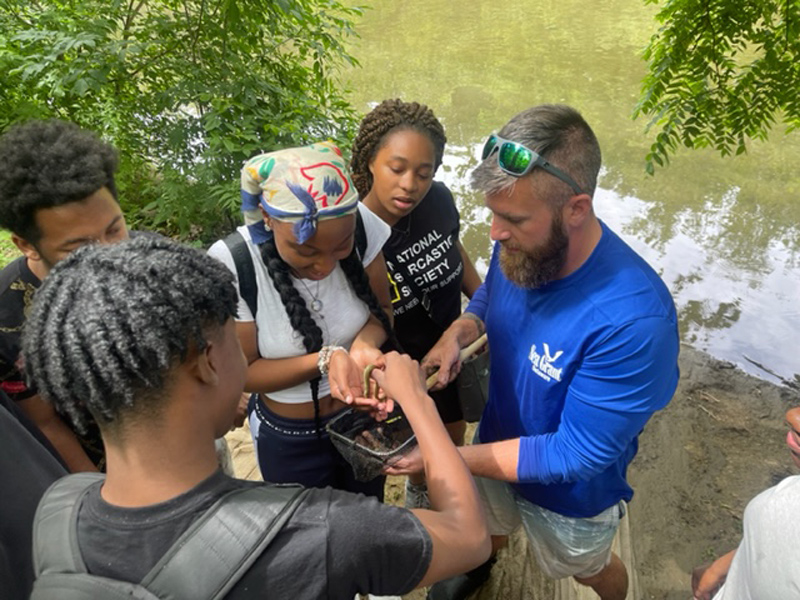 Image of students gathered around a Delaware Sea Grant guide who is holding net reptile